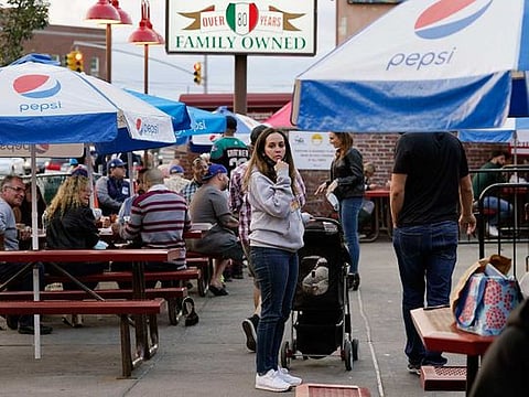 A woman waits in line at L&B Spumoni Gardens during the dinner hour, Sunday, Oct. 4, 2020, in the Bensonhurst/Gravesend section of the Brooklyn borough of New York. Mayor Bill de Blasio said that he has asked the state for permission to close schools and reinstate restrictions on nonessential businesses in several New York neighborhoods, including this one, because of a resurgence of the coronavirus. 