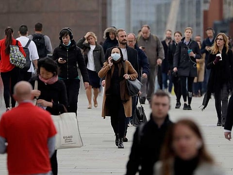 Commuters walk across London Bridge during the morning rush hour towards the offices in the financial district of the City of London, in London, Monday, Oct. 12, 2020. 