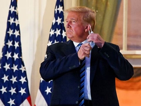 POST-TREATMENT: President Donald Trump pulls off his protective face mask as he poses atop the Truman Balcony of the White House after returning from being hospitalized at Walter Reed Medical Center, October 5, 2020. 