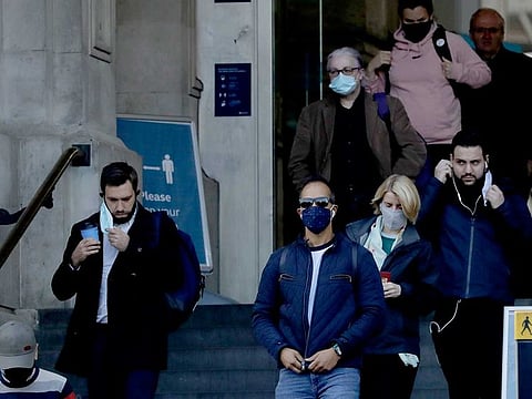 People walk down the steps of the main entrance of Waterloo train station, at which point they are allowed to remove their face coverings, in London, Thursday, Oct. 15, 2020.