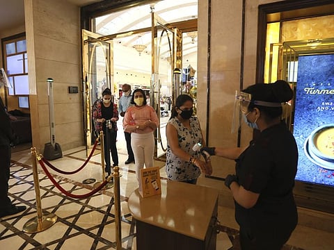 An employee checks the temperature of COVID-19 warriors and their families arriving as cinemas reopen with a special screening for them at the PVR movie theater in New Delh.