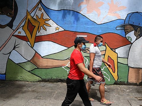 People wearing protective masks to prevent the spread of the coronavirus walk past a mural showing a Philippine flag and Filipinos wearing masks in Manila, Philippines.