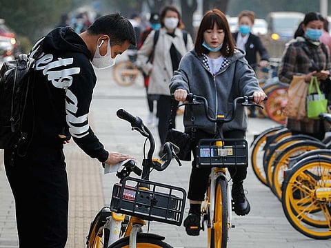 A man wearing a face mask to help curb the spread of the coronavirus uses an alcohol tissue to disinfect a bicycle of bike-sharing companies during the morning rush hour in Beijing, Monday, Oct. 26, 2020. Schools and kindergartens have been suspended and communities are on lockdown in Kashgar, a city in China's northwest Xinjiang region, after more than 130 asymptomatic cases of the coronavirus were discovered.