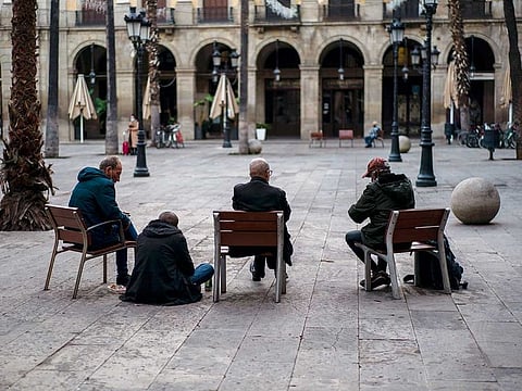 Homeless people sit on an empty square in downtown Barcelona, Spain, Tuesday, Nov. 10, 2020 as Spain continue with new measures against the COVID-19.  