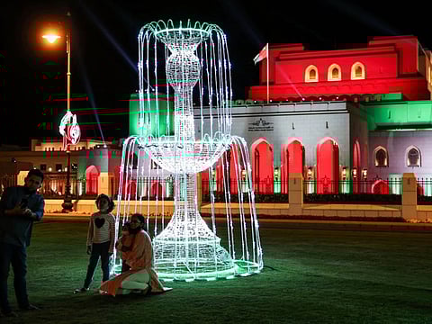 Indian residents of Oman pose for a picture on the lawn before the Royal Opera House Muscat in Oman's capital, lit up with the national colours on the occasion of the Omani national day.