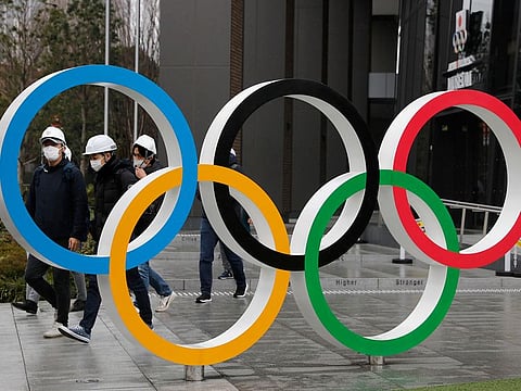 Pedestrians wear masks outside the National Stadium Olympic Rings in Tokyo