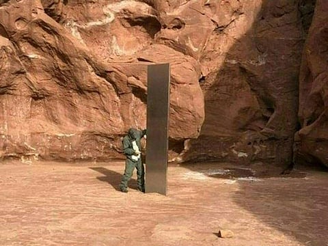 A metal monolith installed in the ground in a remote area of red rock.