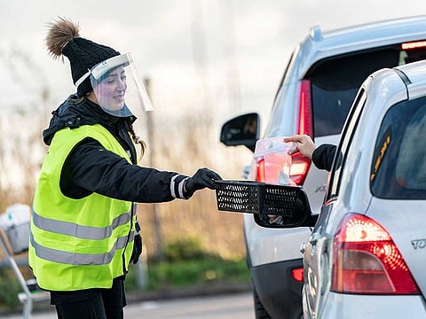A person wearing a protective mask collects coronavirus self tests from people in cars at a testing site in the car park of Svagertorp railway station, amid the coronavirus disease (COVID-19) outbreak, in Malmo, Sweden.