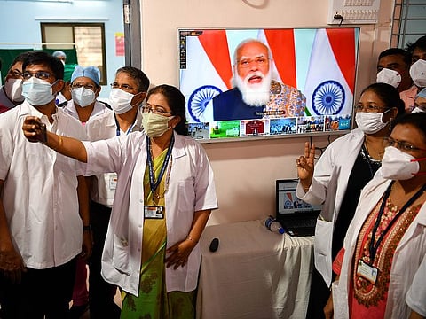 Doctors from the Rajawadi Hospital pose for a selfie as a television broadcasts a live address by India's Prime Minister Narendra Modi before the start of the COVID-19 vaccination drive   