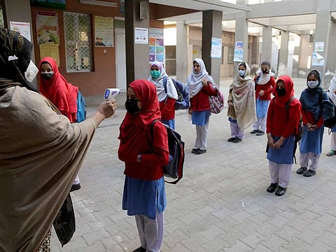 A teacher checks the body temperature of students on their arrival at a school in Peshawar, Pakistan, Monday, Feb. 1, 2021. 