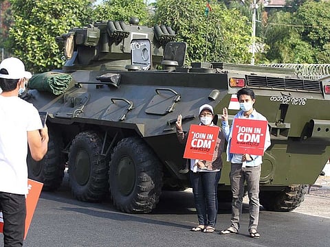 Anti-coup protesters flash the three-fingered salute and hold signs that read "Join in CDM (Civil Disobedience Movement)" while they pose for a photo at the back of an armoured personnel carrier deployed outside the Central Bank of Myanmar building in Yangon, Myanmar on Monday, Feb. 15, 2021. 