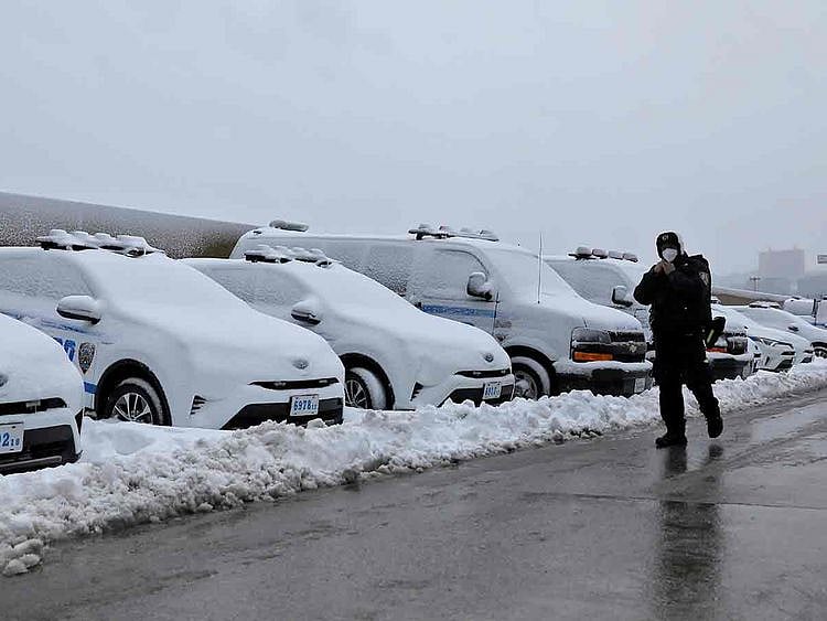 An officer from the New York Police Department (NYPD) walks by a row of police vehicles buried in snow near the Hudson Yards precinct in Manhattan, New York City 