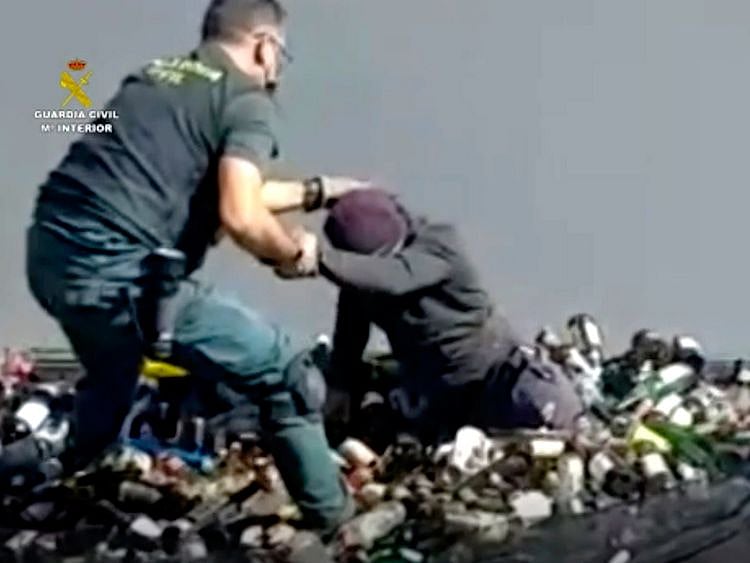 An officer of the Guardia Civil helps a man out from under glass bottles in a container in Melilla. 