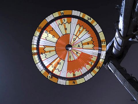 This illustration provided by NASA shows a diagram added over the parachute deployed during the descent of the Mars Perseverance rover as it approaches the surface of the planet on February 18, 2021. Systems engineer Ian Clark used a binary code to spell out “Dare Mighty Things” in the orange and white strips of the 21-meter parachute. 