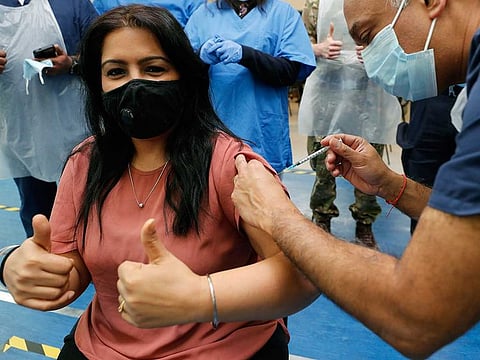 Dr Anil Mehta, surrounded by his team of doctors, administers a dose of the Pfizer vaccine to Geeta Waddon to mark the 10,000th jab in his small practice in London, Sunday, Feb. 28, 2021. 