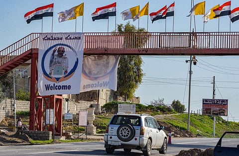 Flags of Iraq and of the Holy See fly on a pedestrian bridge near a large banner showing a sign of welcome for Pope Francis, ahead of his visit to Iraq in the town of Karemlash, about 28km southeast of Iraq's northern city of Mosul, on February 28, 2021. 