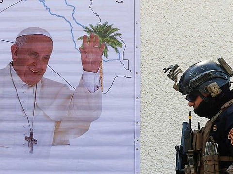 A security man walks near a poster of Pope Francis upon his upcoming visit to Iraq, in Baghdad, Iraq March 3, 2021. 