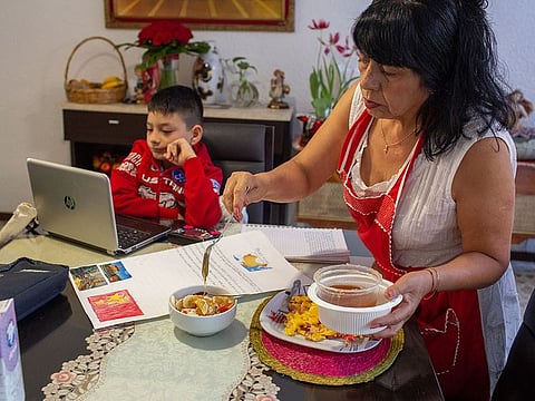 The report says tasks related to meal preparation are especially time-consuming as families now take all of their meals at home, compared to before the pandemic. Seen here is Alicia Ruiz Robles from Mexico preparing breakfast for her grandson while he attends school online