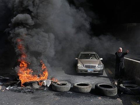A Maronite Christian priest pleads anti-government protesters to let him pass with his vehicle as he stands next to burning tires at a make-shift roadblock in Zouk Mosbeh north of Lebanon's capital Beirut, on March 8, 2021 as they protest against the deteriorating value of the local currency and dire economic and social conditions. 