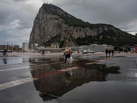 People cross the Gibraltar airport runway towards the border crossing with Spain, backdropped by the Gibraltar rock. 