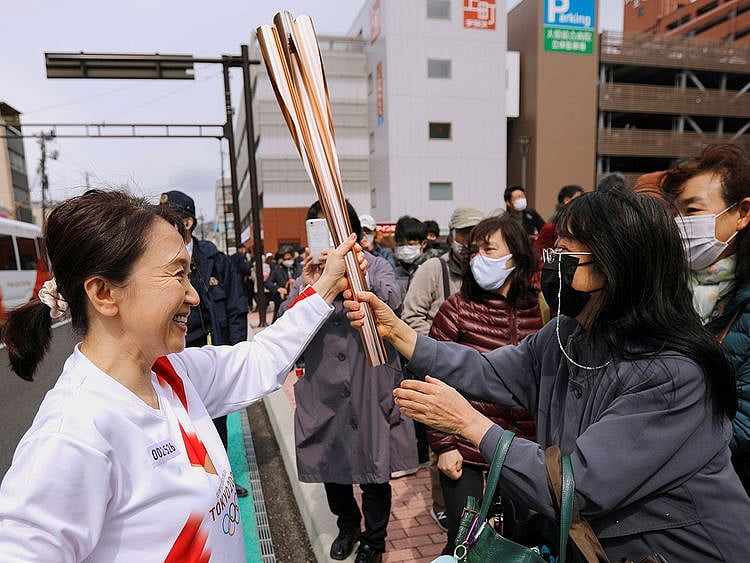 Spectators try to touch the torch carried by torchbearer Junko Ito, after her run during the Tokyo 2020 Olympic torch relay on the second day of the relay in Fukushima