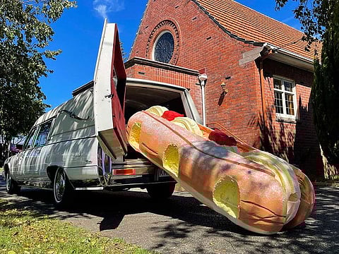 This photo provided by Ross Hall, shows a cream doughnut shaped coffin for the funeral of Phil McLean outside a church in Tauranga, New Zealand on Feb 17, 2021. Auckland company Dying Art makes unique custom caskets which reflect the people who will eventually lay inside them, whether it's a love for fire engines, a cream doughnut or Lego. 