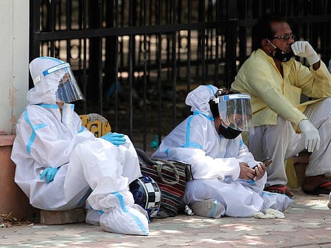 People in personal protective suits wait outside a mortuary to collect the body of their relative who died of coronavirus, in New Delhi, India, Monday, April 19, 2021. 