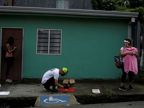 A worker sprays paint on a stencil indicating social distancing on the floor of a bus stop, as the spread of the coronavirus disease continues, in San Jose, Costa Rica.