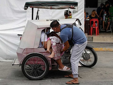 A man carries a sick woman from a pedicab as they bring her to the emergency area of the hospital that is crowded with suspected COVID-19 patients in Manila
