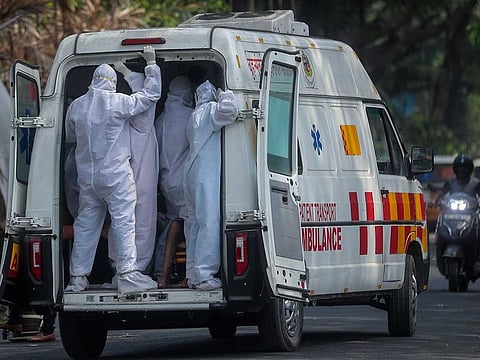 Health workers stand on the back of an ambulance as they transport patients at a COVID-19 field hospital in Mumbai, India (File)