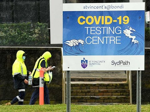 Medical officers walk past a sign board of COVID-19 testing centre on Bondi Beach in Sydney on May 6, 2021, as the administration implemented restrictions after new cases of community transmission. 