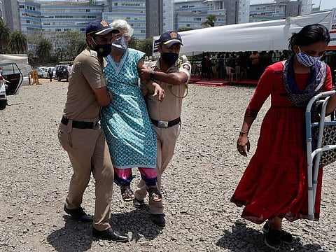 Police personnel help an elderly woman outside a vaccination centre in Mumbai, India 