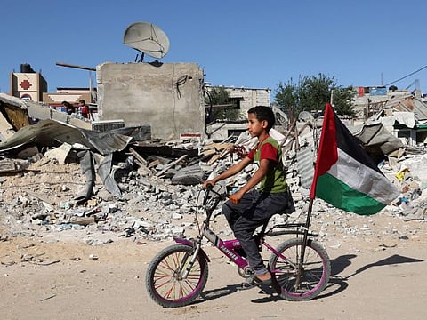 A Palestinian child rides his bicycle in front of the ruins of a building destroyed during recent Israeli bombing in Rafah, in the southern Gaza Strip, on May 26, 2021. - Diplomatic efforts are underway to solidify a fragile Egypt-brokered truce that halted the fighting, with plans to rebuild the Gaza Strip where Israeli air strikes damaged infrastructure and levelled buildings. (Photo by SAID KHATIB / AFP)