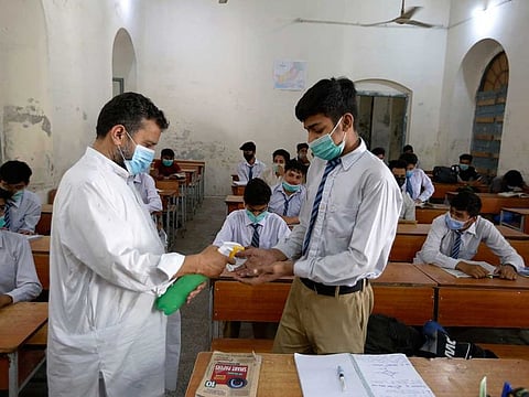 A teacher sanitises the hand of a student to help prevent the spread of the coronavirus while he with others attend class at a school, in Lahore, Pakistan, Monday, May 31, 2021. 