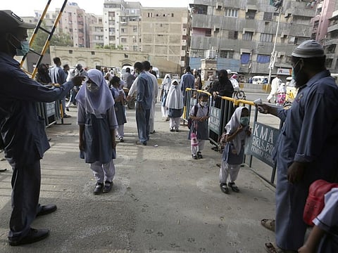 Workers check the body temperature of students upon their arrival at a school, in Karachi on June 21, 2021. Authorities of Pakistan’s Sindh province reopened educational institutes following a steady decrease in deaths and infections from the coronavirus. 