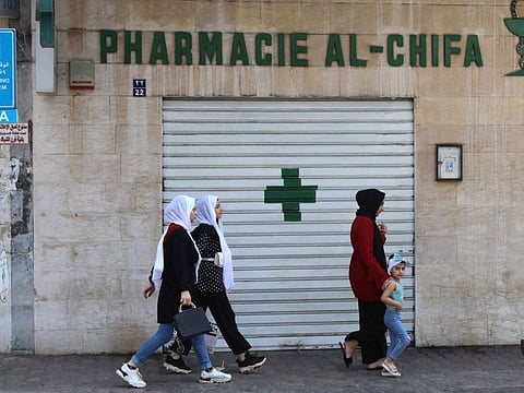 People walk in front of the shuttered door of a pharmacy in Beirut during a nationwide strike of pharmacies to protest against a severe shortage of medicine, on July 9, 2021. 