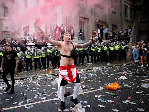An England fan waves a smoke bomb in front of a line of police officers monitoring England supporters standing on the edge of Trafalgar Square during a live screening of the Euro 2020 football final between England and Italy, in central London on July 11, 2021.