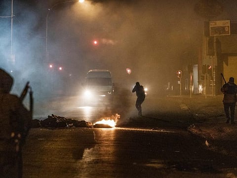 A South Africa Police Service (SAPS) officer aims his rifle at an incoming minivan bringing it to a stop in Jeppestown, Johannesburg, on July 12.