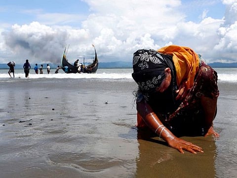 An exhausted Rohingya refugee woman touches the shore after crossing the Bangladesh-Myanmar border by boat through the Bay of Bengal, in Shah Porir Dwip, Bangladesh