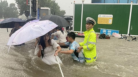 A traffic police officer guides residents to cross a flooded road with a rope during heavy rainfall in Zhengzhou on July 20, 2021. 