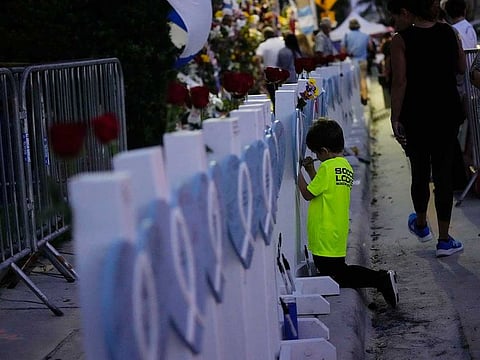 David Barragan, 5, writes a message on a wooden heart dedicated to Luis Bermudez, 26, one of the scores of victims of the Champlain Towers South condo building collapse, as people gathered for a multi-faith vigil near the site where the building once stood, Thursday, July 15, 2021, in Surfside, Fla. 