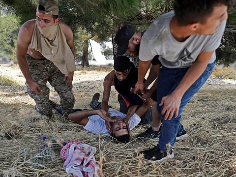 Volunteers tend to a man who as they help firefighters to extinguish a forest fire in the Qubayyat area of northern Lebanon's remote Akkar region on July 29, 2021. A Lebanese teenager was killed as he joined volunteers battling devastating forest wildfires in northern Lebanon, where firefighters were struggling to protect homes from the blaze.  
