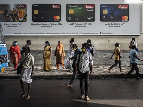 People wait to board buses as others walk in Kochi, Kerala state, India, on August 5, 2021. 
