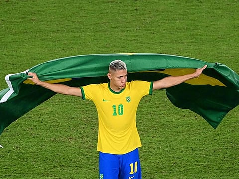 Brazil's Richarlison, wrapped in a Brazilian flag, celebrates after winning the Tokyo 2020 Olympic Games football competition men's gold medal match by defeating Spain 2-1 in extra time at Yokohama International Stadium in Yokohama, Japan.