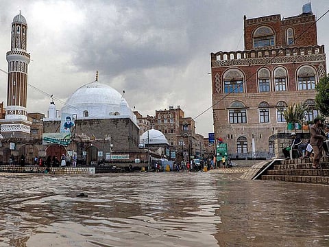 People sit by a mosque along the bank of a flooded drainage canal following heavy rainfall in the old city of Yemen's capital Sanaa on August 3, 2021. 