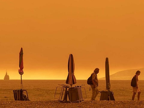 People walk on the beach during wildfires as thick smoke covers the whole area in Pefki, on the island of Evia, Greece, on Sunday, Aug. 8, 2021.