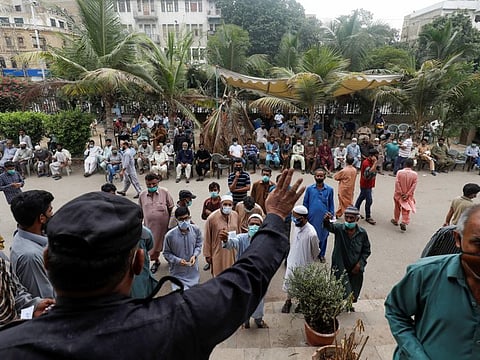 An officer calls on residents with their registration numbers, who are waiting to receive a dose of COVID-19 vaccine, outside a vaccination facility in Karachi, on August 4, 2021.  