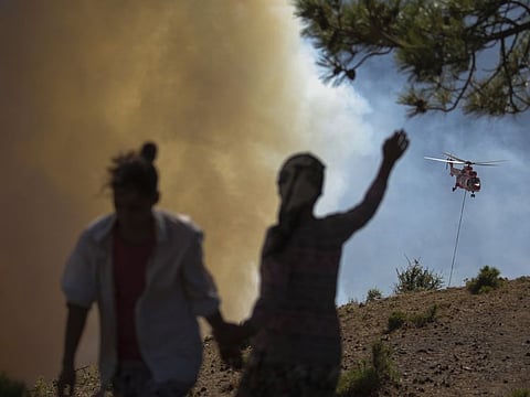 People watch as a helicopter participates in a wildfire extinguishing operation, in Koycegiz, Mugla, Turkey, on August 9, 2021.  