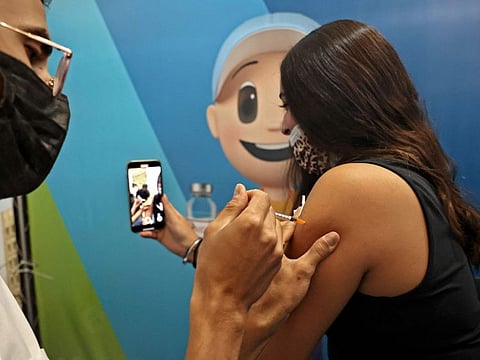 A young Israeli woman photographs herself as she receives a dose of the Pfizer-BioNTech vaccine against the coronavirus at a Clalit Health Services station set up inside Cinema City complex in Jerusalem, on August 11, 2021. 