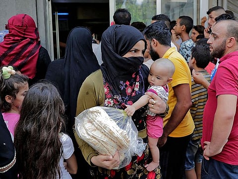 A woman carrying a toddler leaves a bakery with a bag of bread as people wait for their turn, in the neighbourhood of Nabaa in the Lebanese capital Beirut's southern suburbs amidst a wave of shortages of basic items due to a severe economic crisis.